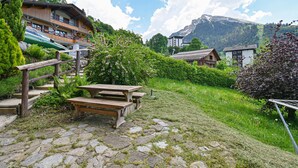 A stone-paved patio with picnic tables, a wooden staircase, and a view of mountain houses and a mountain in the background. - Ground-Floor Apartment for 4, 50 m from the Slopes in La Clusaz (La Clusaz)