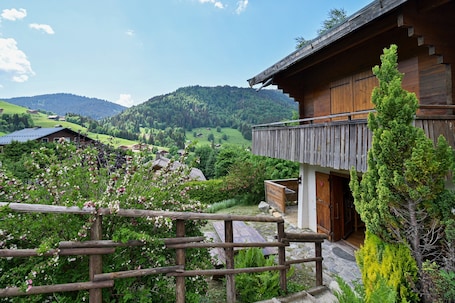A wooden cabin with a balcony overlooking a lush valley and distant mountains.. Ground-Floor Apartment for 4, 50 m from the Slopes in La Clusaz