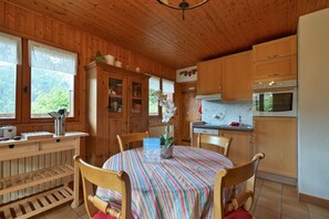 Un intérieur en bois comprenant une table à manger, des chaises, un coin cuisine avec des placards et une fenêtre avec des rideaux.