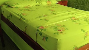 Een eenpersoonsbed met een bloemenbedekker in een kamer met groene wanden en een gestructureerd paneel.