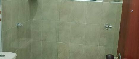A bathroom with a toilet, a shower area, and a shelf with toiletries.