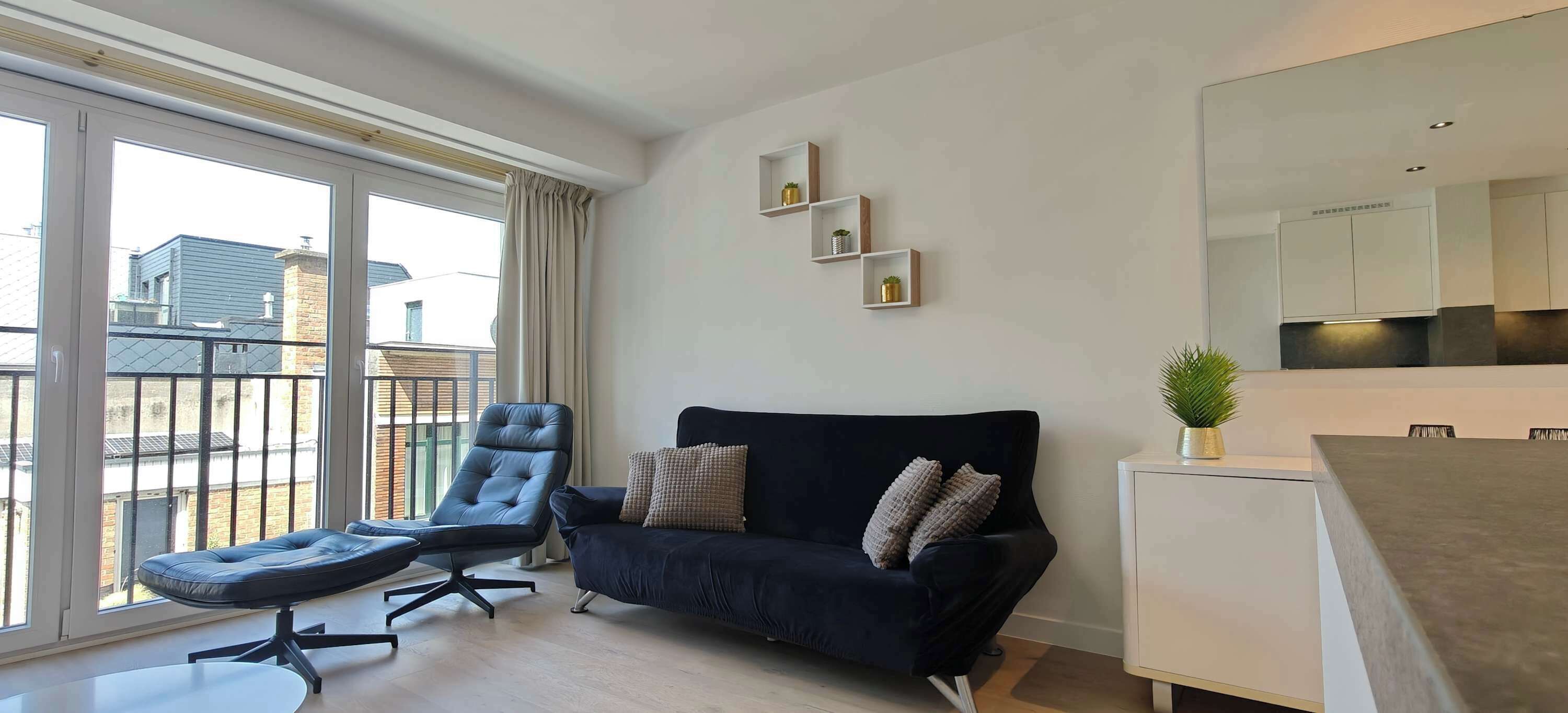 Een moderne woonkamer met een bank, een fauteuil, een kleine tafel en een plant in pot.