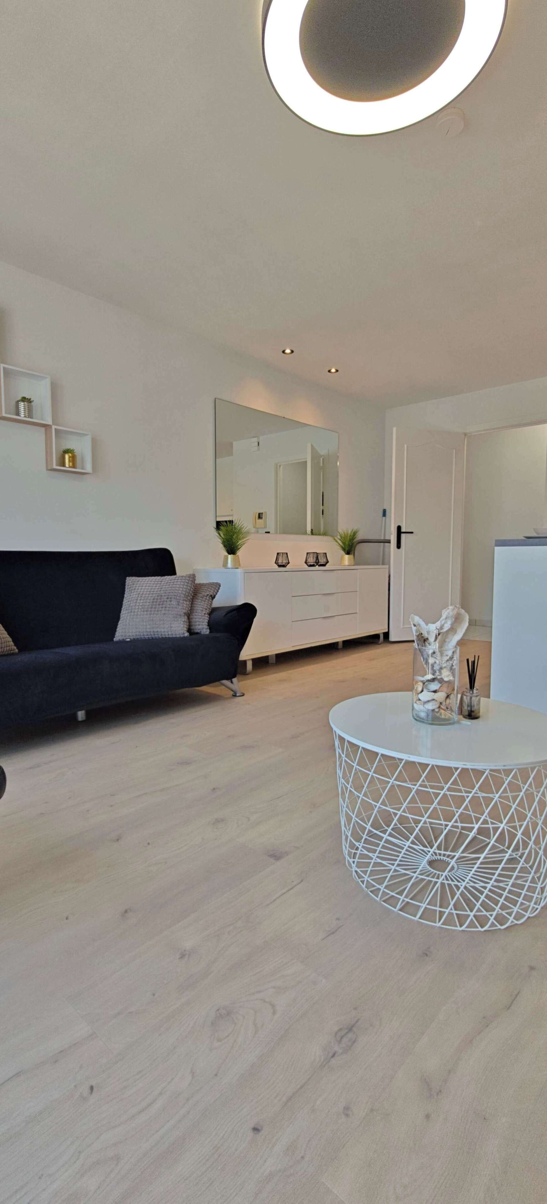 A modern living room with a black sofa, a round white table, and a white cabinet with a mirror.