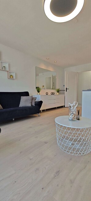 A modern living room with a black sofa, a round white table, and a white cabinet with a mirror. - Central Ostend Apt: Family-Friendly Comfort (Oostende)