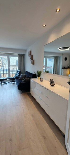 A modern living room with a sofa, a dining table, and a large mirror. - Central Ostend Apt: Family-Friendly Comfort (Oostende)