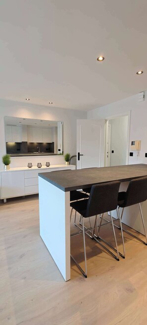 A modern kitchen with white cabinets, a central island, and recessed ceiling lights. - Central Ostend Apt: Family-Friendly Comfort (Oostende)