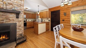 Una cocina con chimenea de piedra, armarios de madera, una mesa de comedor de madera y vistas por una ventana.