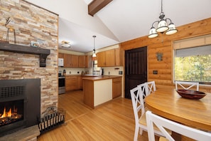 A kitchen with a stone fireplace, wooden cabinets, a central island, and a dining area with a wooden table and chairs.