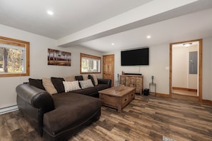 A living room with a sectional sofa, wooden flooring, a flat-screen TV, and a wooden cabinet.