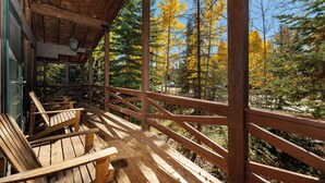 Una terraza de madera con bancos, barandilla y vistas a un bosque de árboles con colores otoñales.