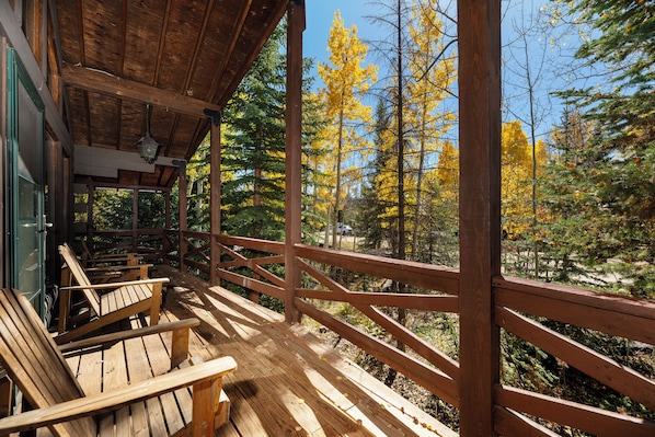 A wooden deck with benches, a railing, and a view of a forest with autumn-colored trees.