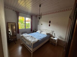A bedroom with a single bed, a nightstand, a chair, a window with curtains, and a chandelier. - 3-Bedroom House for 6 People in Mimizan (Mimizan)