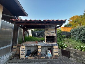 An outdoor brick barbecue area with a chimney, a metal grill, and a small table. - 3-Bedroom House for 6 People in Mimizan (Mimizan)
