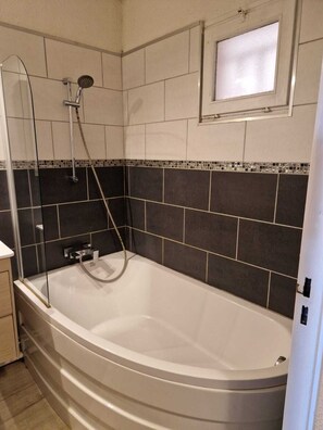 Ein Badezimmer mit einer freistehenden Badewanne, einer Duschbrause und einem kleinen Fenster über der Wanne.