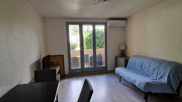 Ein Zimmer mit Esstisch, einer Couch, einem Sessel, einem Deckenventilator und einer Schiebetür zu einem Außenbereich.