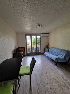 Ein Zimmer mit Esstisch, einer Couch, einem Sessel, einem Deckenventilator und einer Schiebetür zu einem Außenbereich.