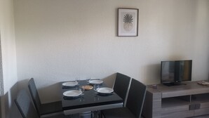 Ein Essbereich mit einem Tisch für vier Personen, einem Fernseher auf einem Schrank und einem gerahmten Bild an der Wand.