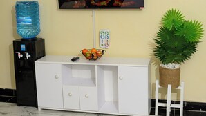 A television mounted on a wall, a water dispenser, a fruit bowl, a white cabinet, and a potted plant. - Lovely 2-bedroom apartment in beautiful Thika for a relaxing stay (Thika)