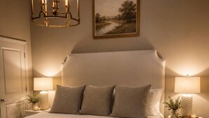 Un dormitorio con una cama grande, dos mesitas de noche con lámparas, una araña y un cuadro de un paisaje en la pared.