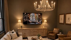 Una sala de estar con un amplio sofá modular, una mesa de centro, un televisor montado en la pared y una araña.