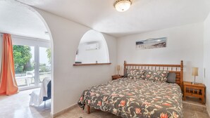 Een slaapkamer met een bed, nachtkastje, lamp, schilderij en uitzicht op het buitenleven.