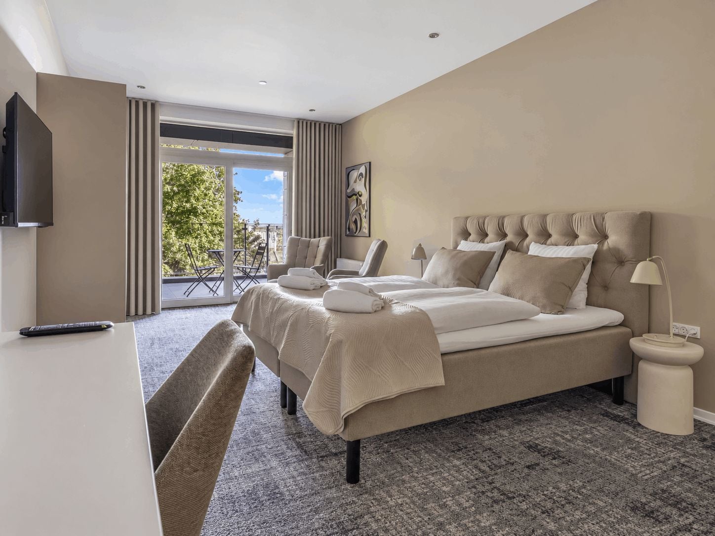 A hotel room with a large bed, a TV, a desk, and a balcony with a view.
