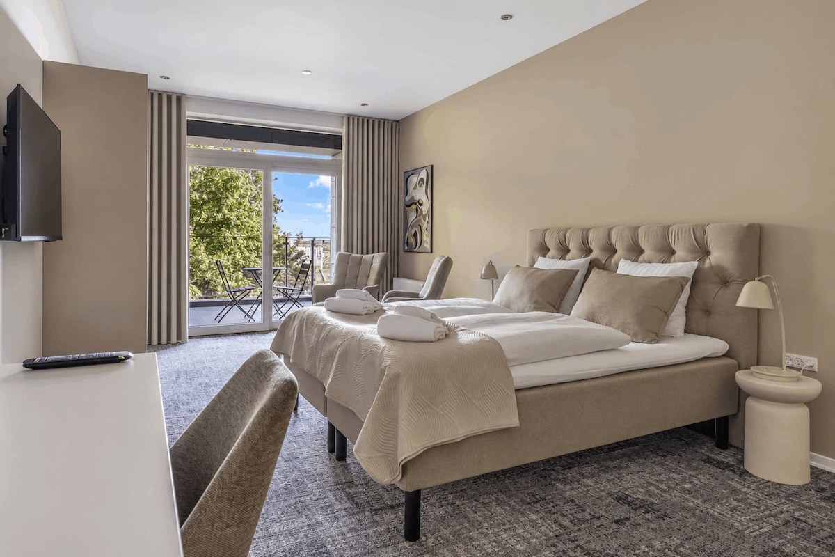 Habitación de hotel con una cama grande, televisión, escritorio y balcón con vistas.