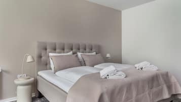 Una cama bien hecha con cabecera, una lámpara de noche y una toalla doblada sobre la cama.