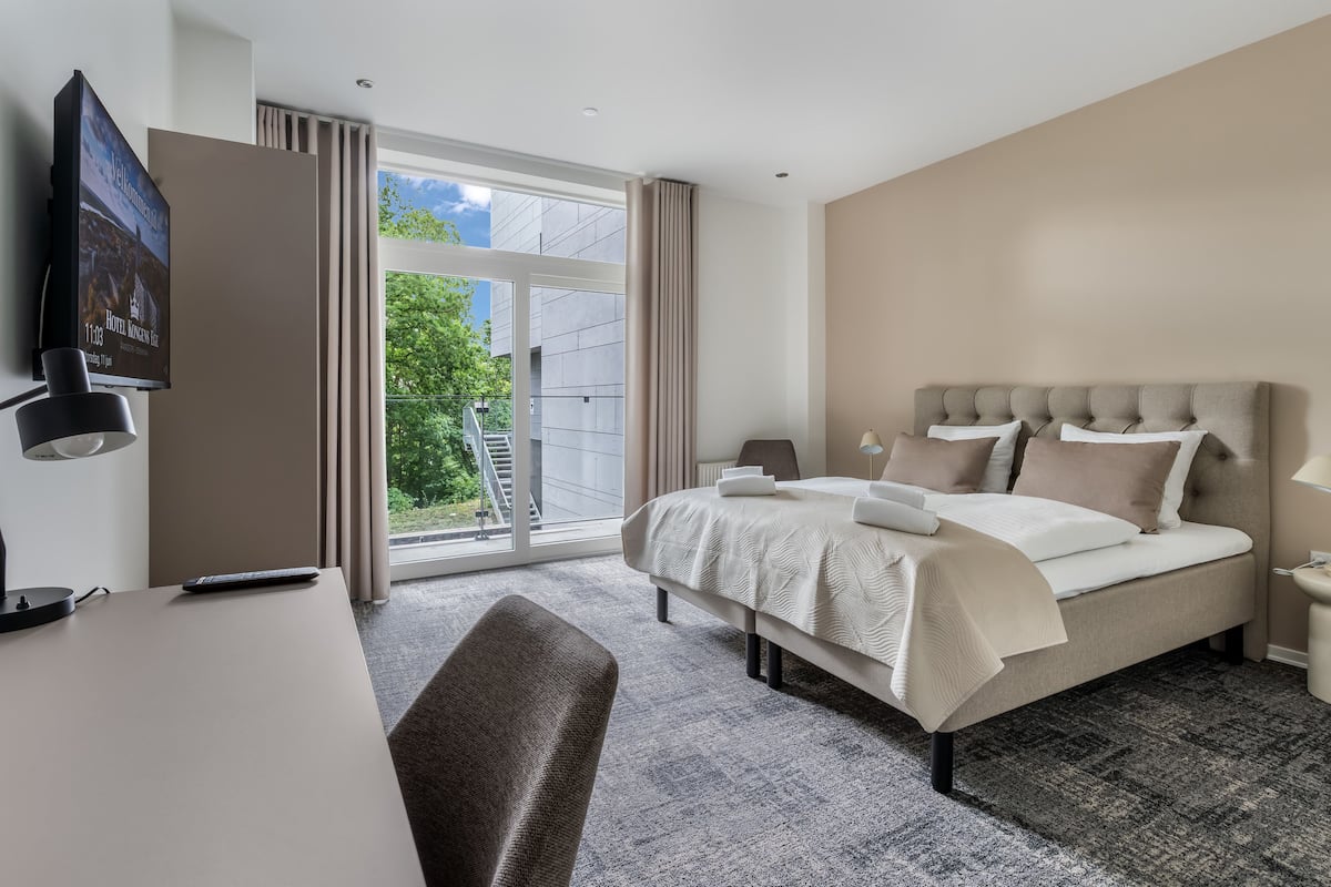 Una habitación de hotel con cama, escritorio, silla y televisión en la pared.