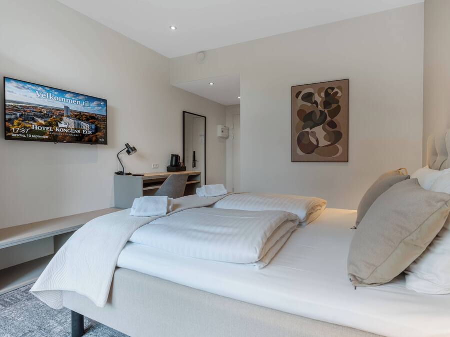 A modern hotel room with a large bed, a desk, and a flat-screen TV displaying a welcome message.