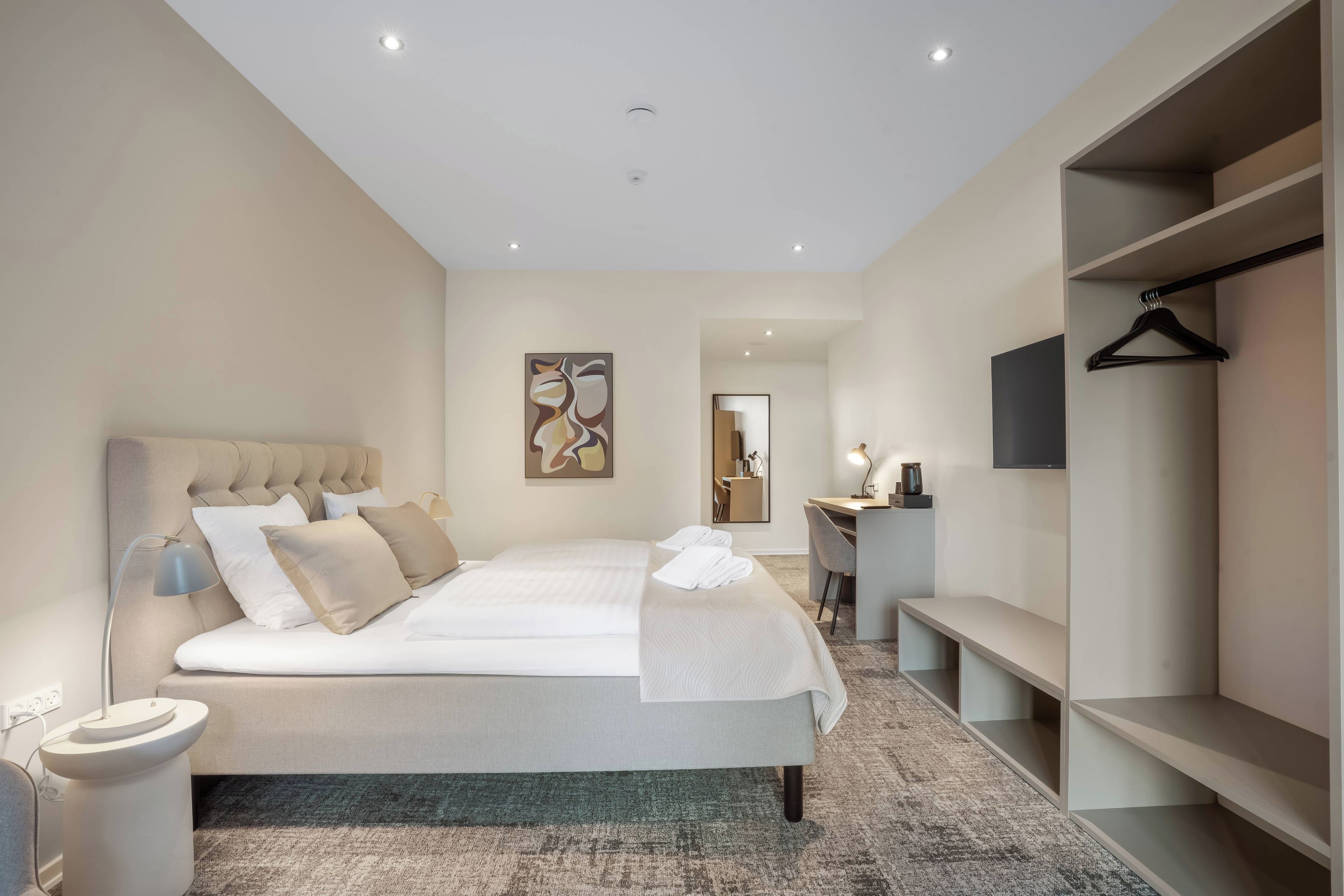Una habitación de hotel moderna con una cama grande, un escritorio, una silla y un televisor montado en la pared.