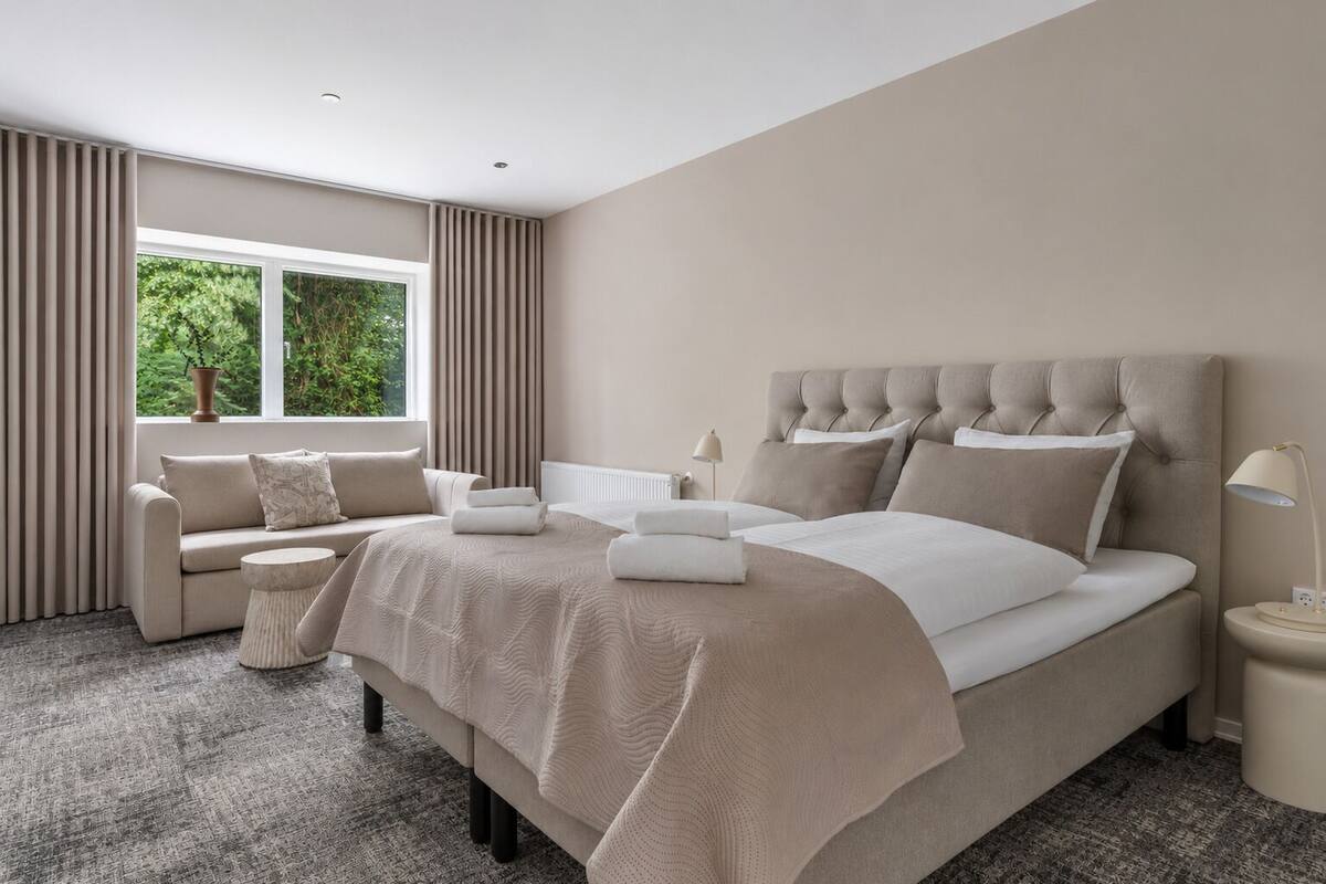 Un dormitorio moderno con una cama grande, un sofá, una mesita de noche y una ventana con cortinas.