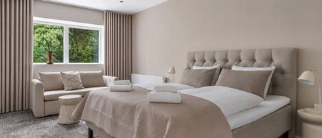 A modern bedroom with a large bed, a sofa, a side table, and a window with curtains.
