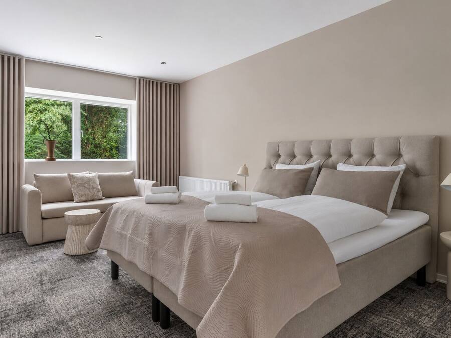 Un dormitorio moderno con una cama grande, un sofá, una mesita de noche y una ventana con cortinas.