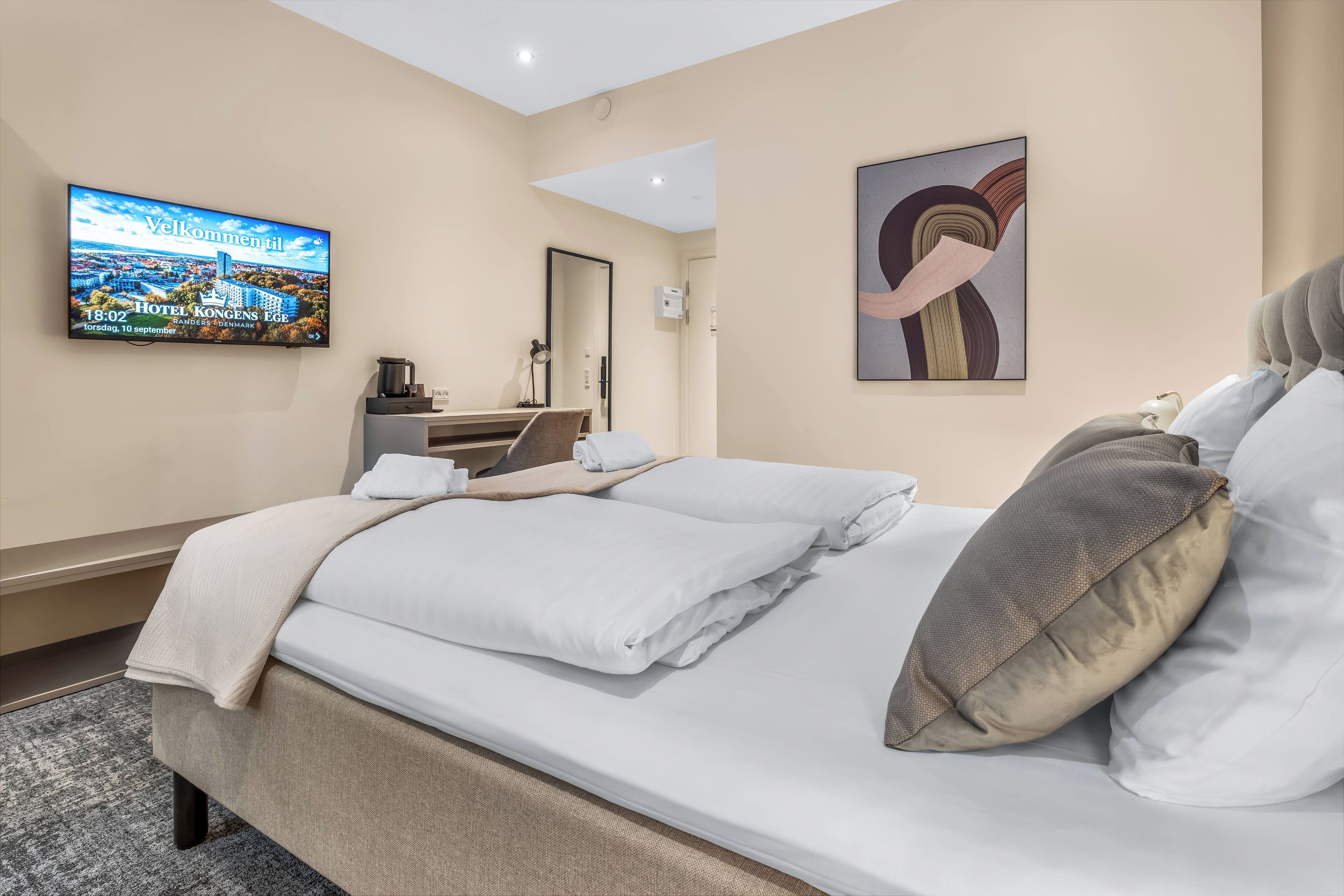 A hotel room with a bed, a flat-screen TV, a desk with a lamp, and a painting on the wall.