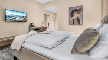 A hotel room with a bed, a flat-screen TV, a desk with a lamp, and a painting on the wall.