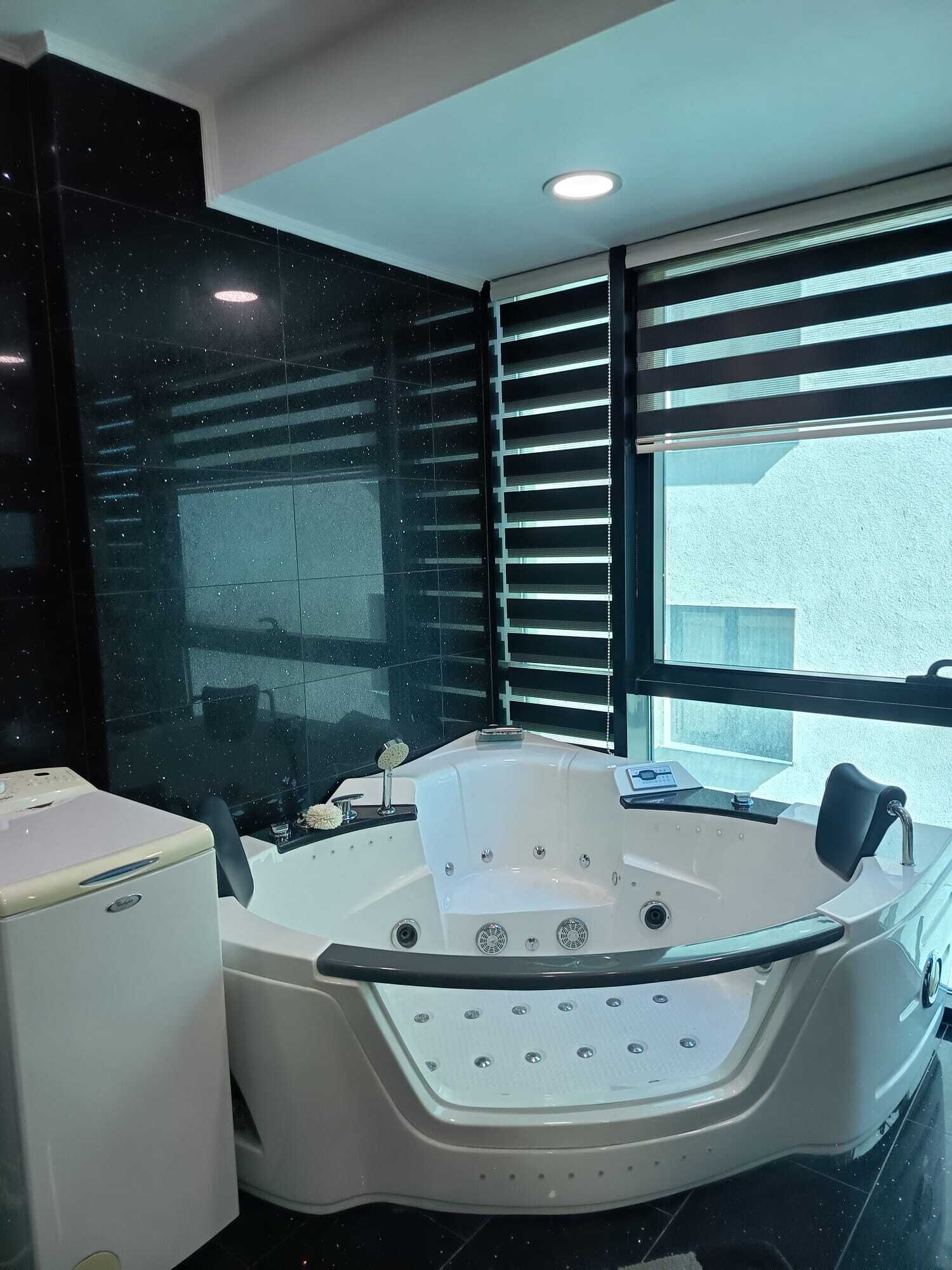 Une salle de bain moderne avec une grande baignoire, des toilettes et une fenêtre équipée de stores.