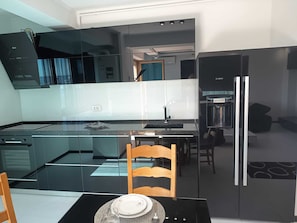 A modern kitchen with a glass island, stainless steel appliances, and a dining area with a wooden chair. - Florence Luxury Apartment Mamaia Beach Constanta Romania (Mamaia-Sat)