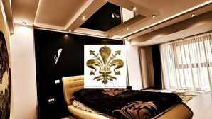 Ein modernes Schlafzimmer mit einem bogenförmigen Bett, Einbauleuchten und einem großen Fenster mit Vorhängen.