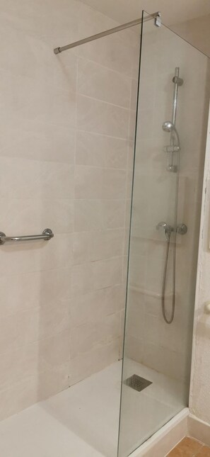 En dusch med glasväggar, ett handhållet duschmunstycke, en väggmonterad blandare och ett handhållet duschmunstycke.