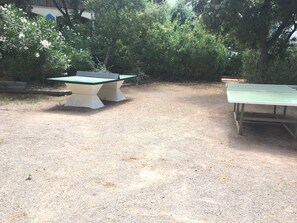 Ett bordtennisbord placerat utomhus på ett område med grusunderlag, omgivet av tät vegetation.