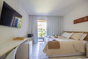 Ein Hotelzimmer mit Bett, Schreibtisch, Fernseher und einem Balkon mit Vorhängen.