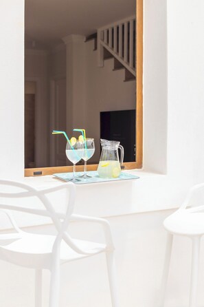 Ein weißer Tisch mit zwei Gläsern eines klaren Getränks, einer Karaffe und einem Fenster mit Blick auf eine Treppe.