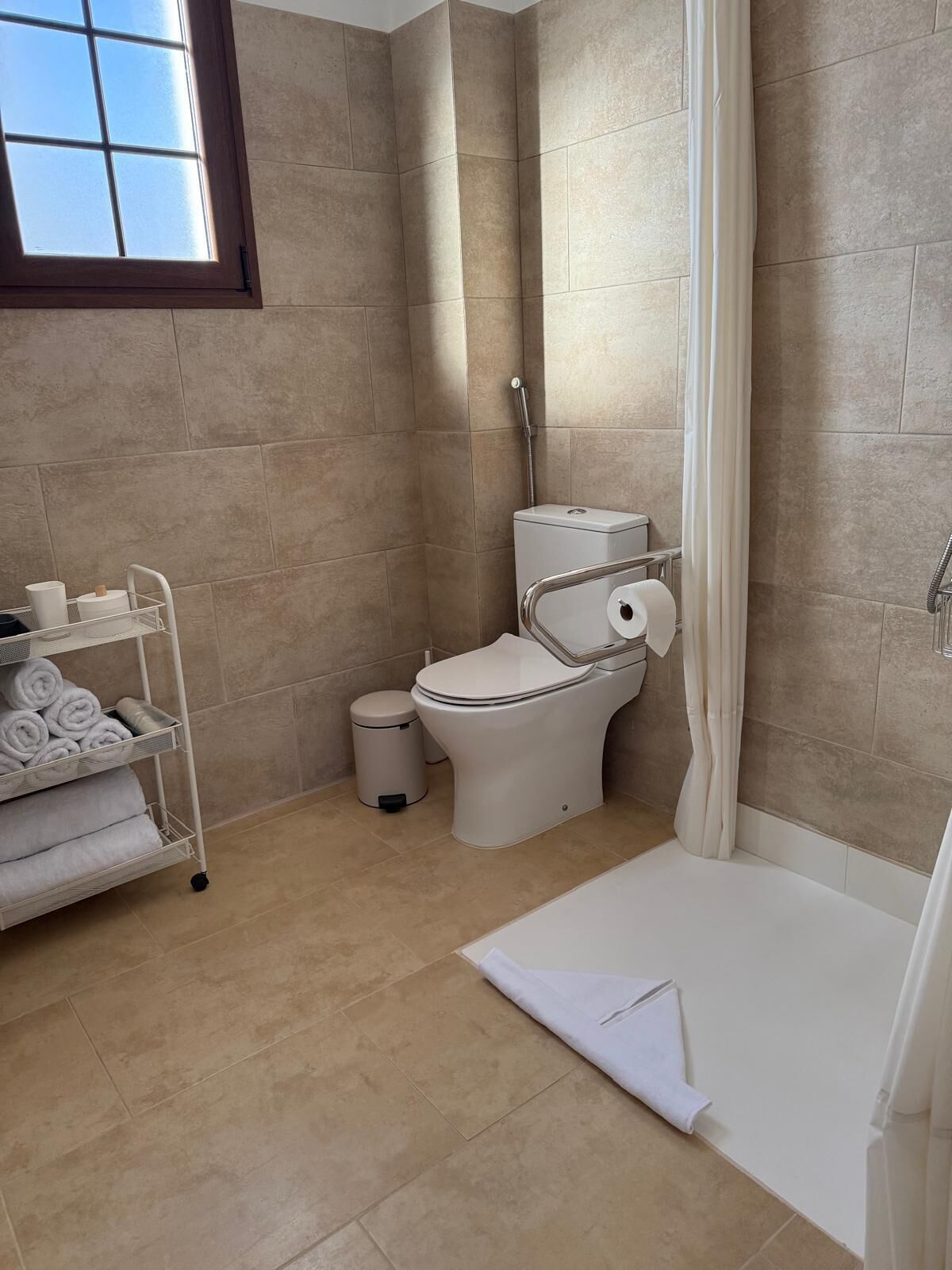 Een badkamer met een toilet, een douche en een handdoekrek met handdoeken.