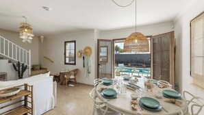 Comedor con una mesa redonda dispuesta para cuatro personas, sillas blancas y vista a una piscina exterior.