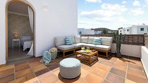 Un balcón con sofá, reposapiés y una planta de cactus.