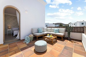 Ein Balkon mit einer Couch, Hocker und einer Kakteenpflanze.