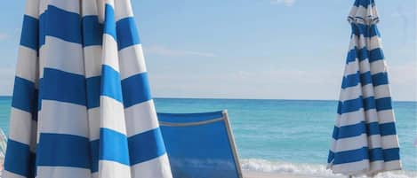 Une scène de plage avec deux parasols rayés et une chaise de plage bleue.