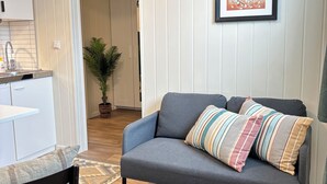 A living room with a grey sofa, a small table, a potted plant, and a framed abstract art piece on the wall. - Rygge Apartments (Moss)