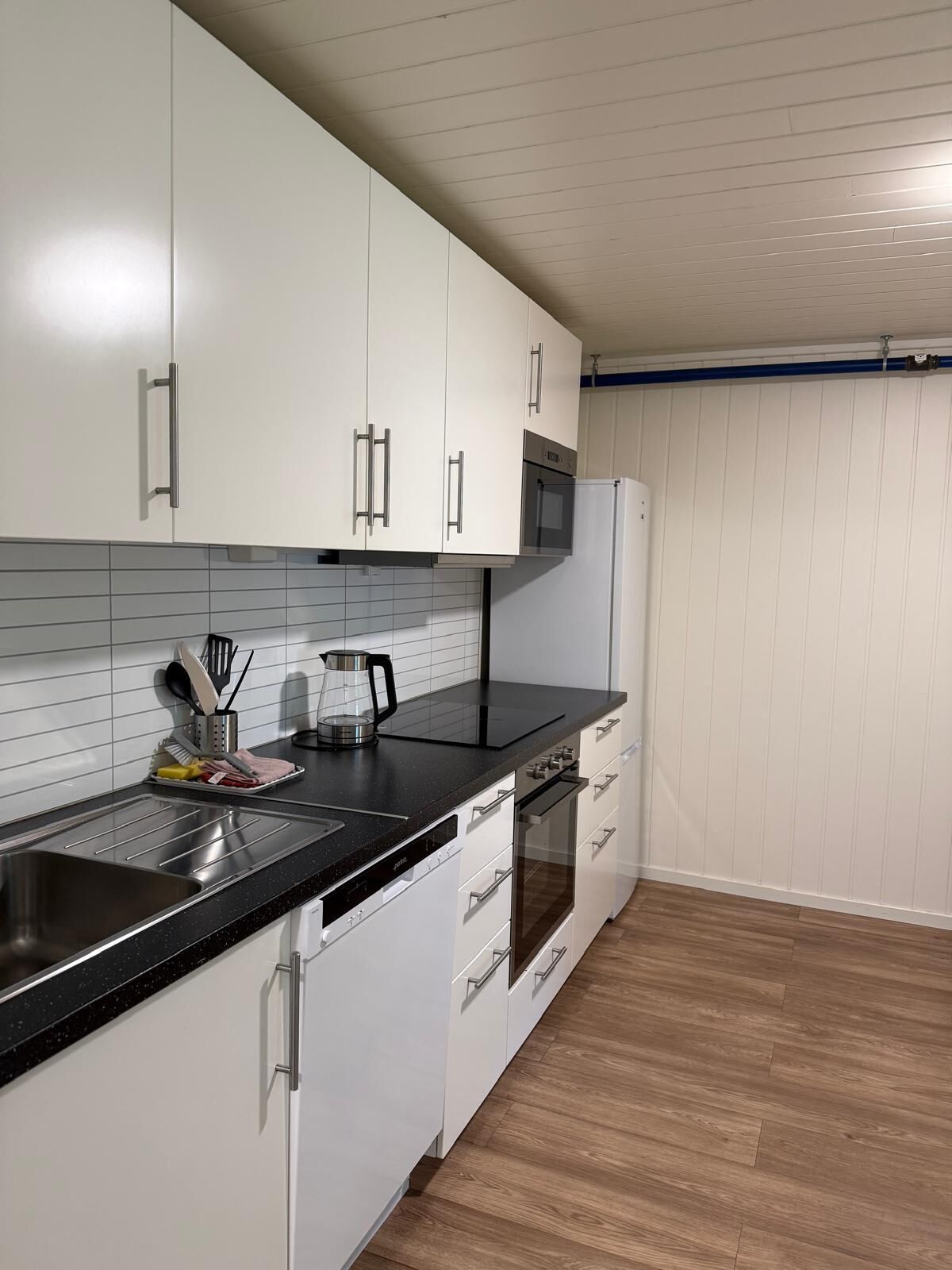 Eine moderne Küche mit weißen Schränken, einer schwarzen Arbeitsplatte, Edelstahlgeräten und Holzböden.